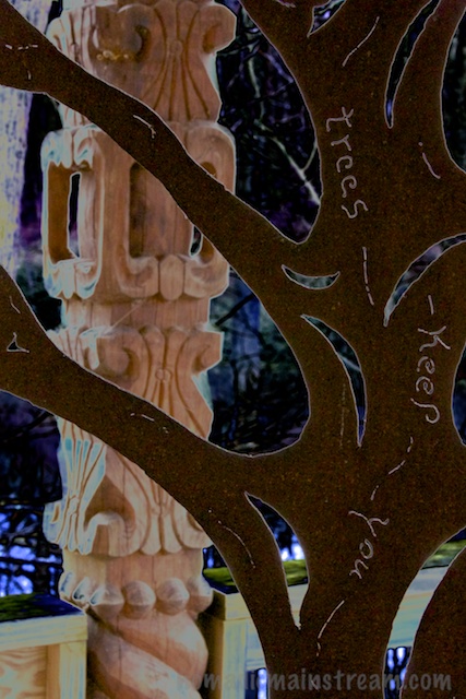 Looking through a metal cutout on a treehouse door at an intricately carved post